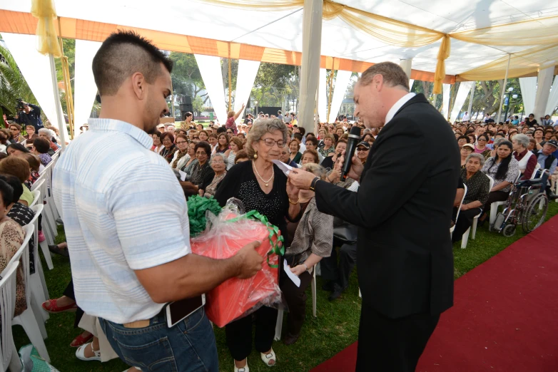 a man in a tuxedo handing someone a present at a convention