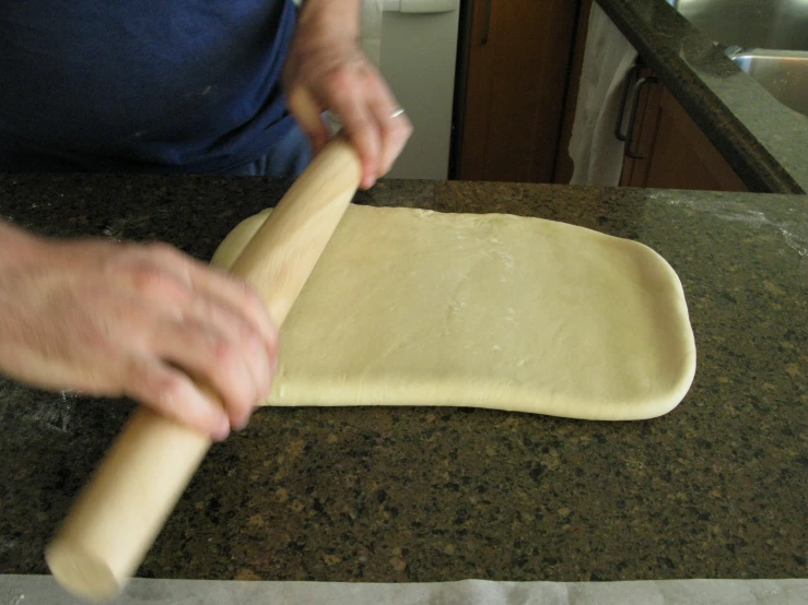 a hand rolling dough from a long bar