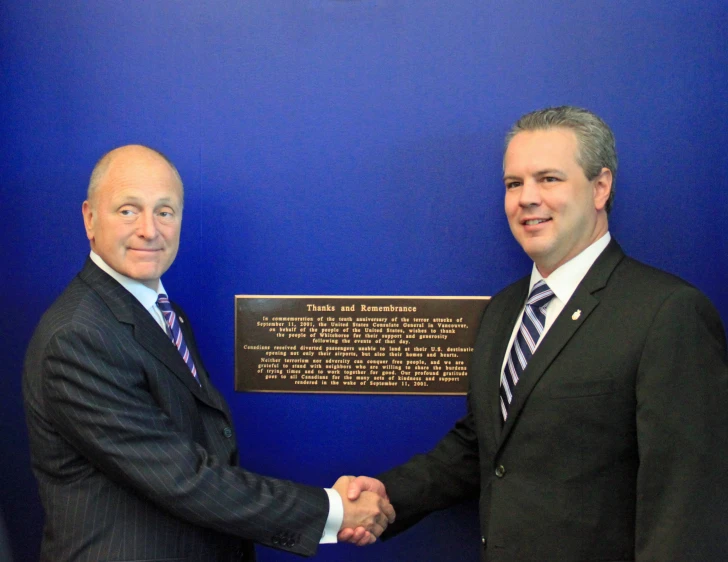 two men in business attire shaking hands next to a plaque