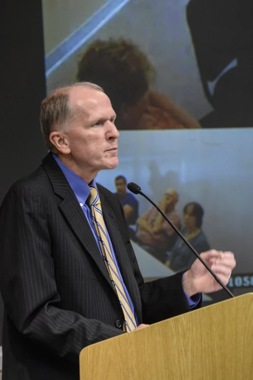 a man is speaking at the podium in front of a screen