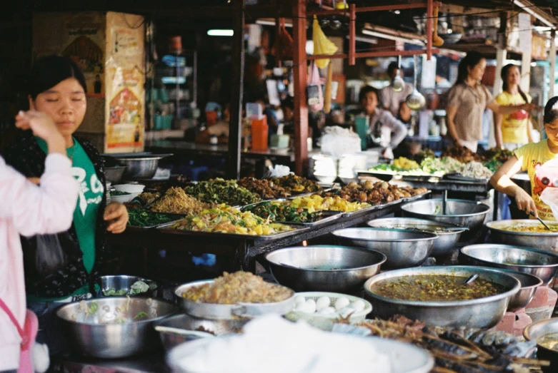 there are people standing at a market selling many foods