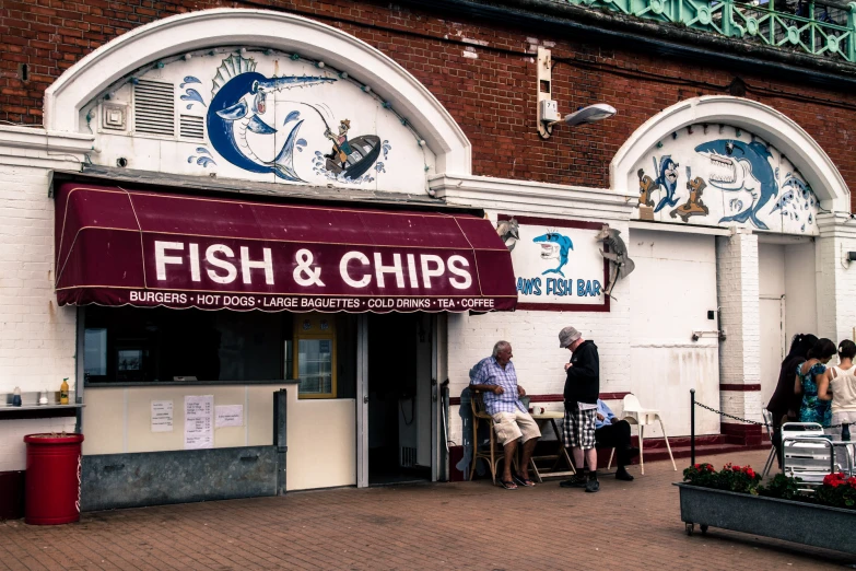 two people sitting at tables outside of a fish and chips restaurant