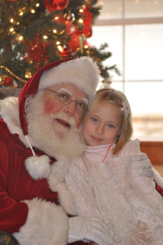 a little girl standing next to a santa clause