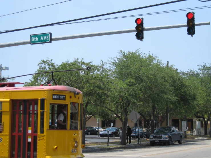 a yellow tram sits in the middle of the street, behind a red light