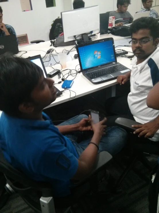 a young man sitting at a computer desk with another guy