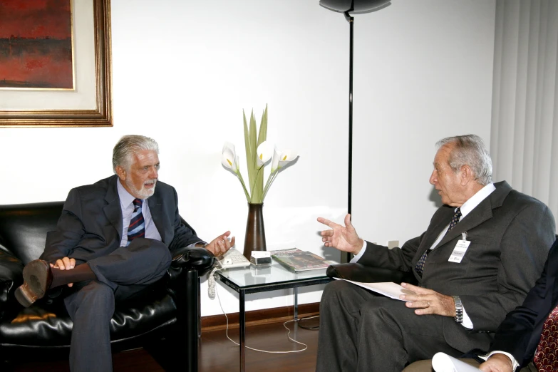 two older men sitting in chairs talking and one is holding his hand out