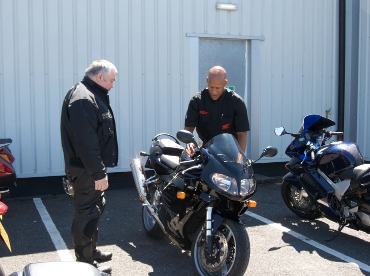 two men standing near motorcycles next to a building