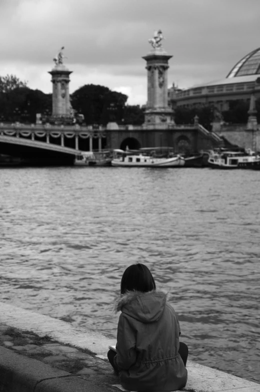 a girl sitting alone on the curb near the water