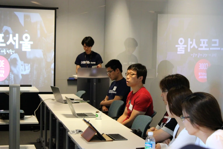 a group of people sitting at a table watching a presentation