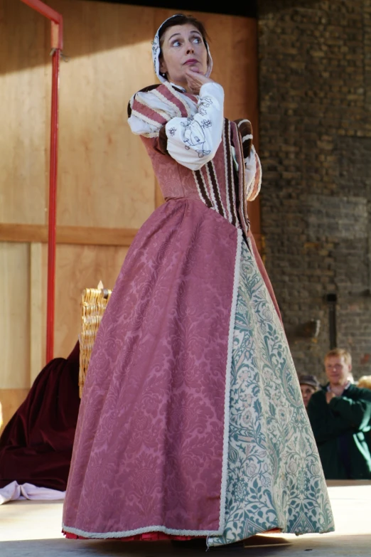 a woman in a pink gown on stage with her hand up to her face