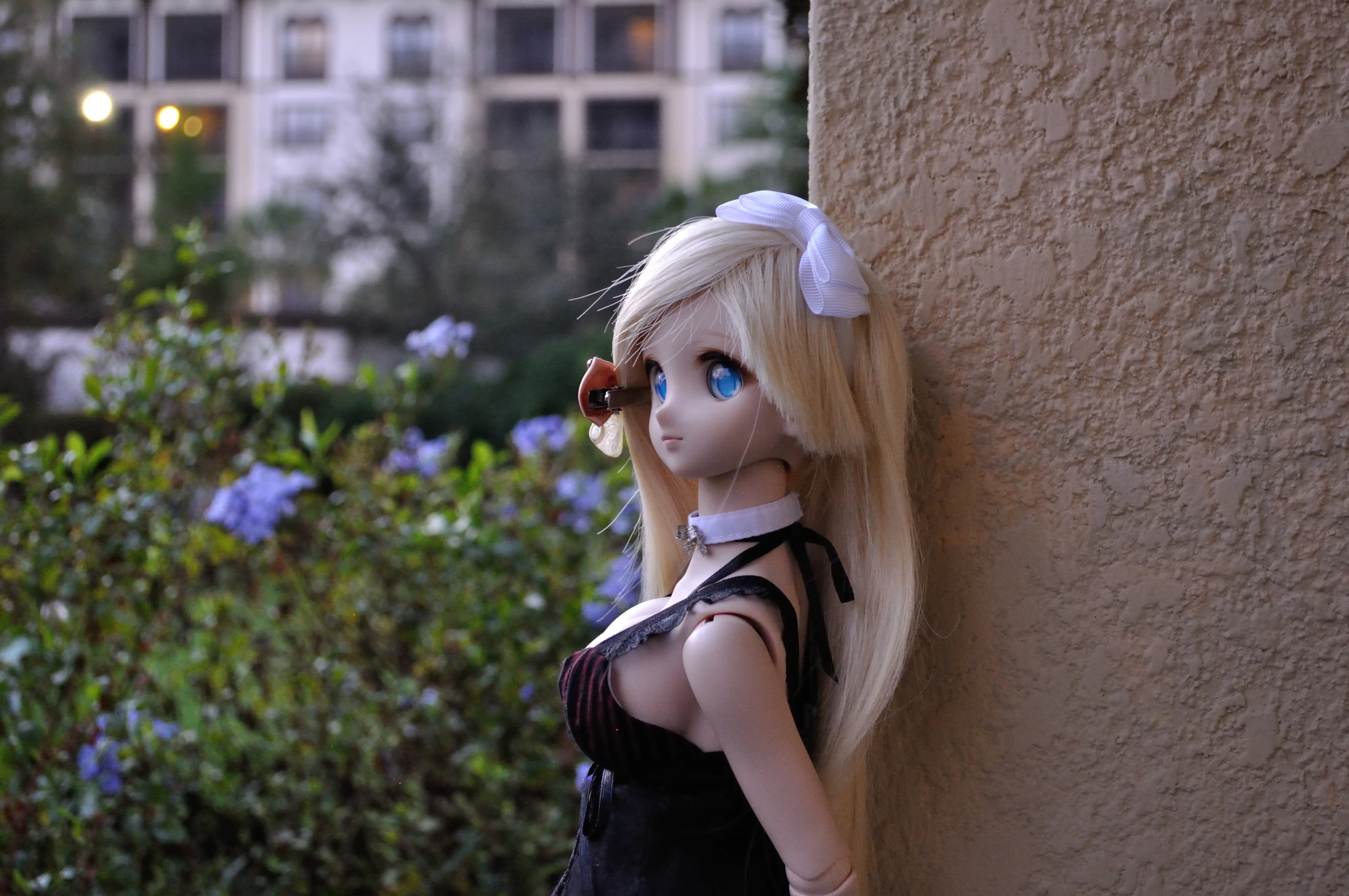 a doll dressed in a little black dress leaning against the side of a wall