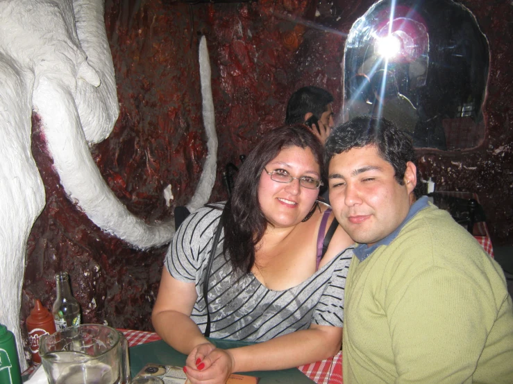 a man and woman sitting in a restaurant with an elephant sculpture behind them