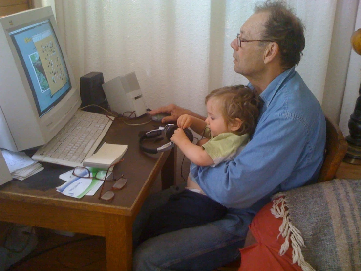 a man sitting on a couch with his young child at a computer desk