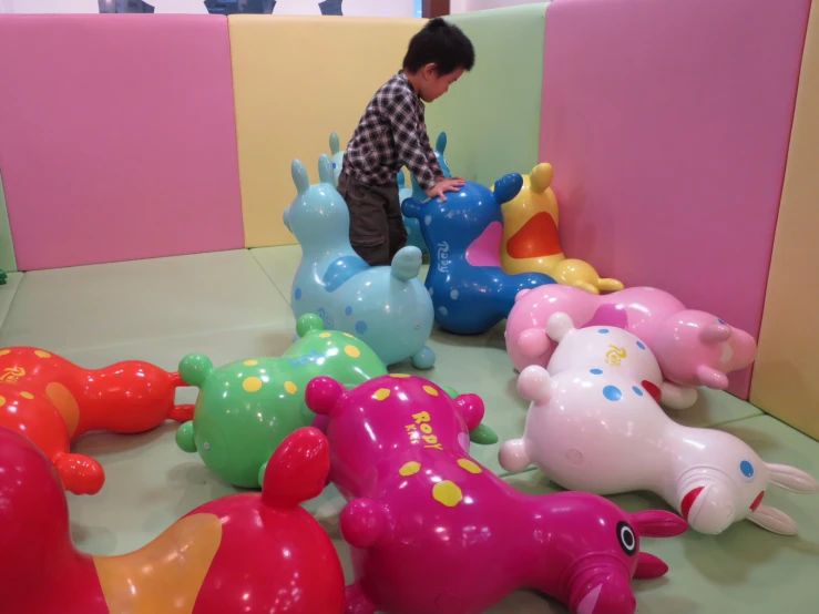 a little boy plays with many fake dinosaurs in a room