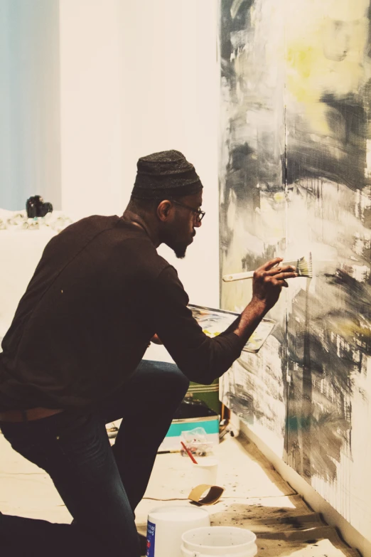 a man with glasses is kneeling down and painting a canvas