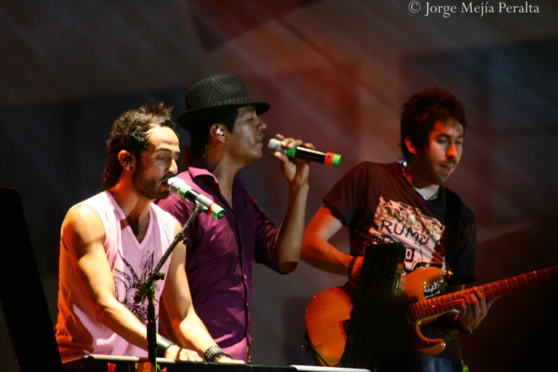 three guys with hats on and one holding a guitar are performing