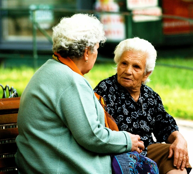 a woman with white hair sits on a bench next to a woman