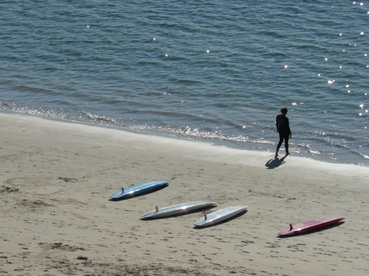 surfboards lay on the beach as a man walks away