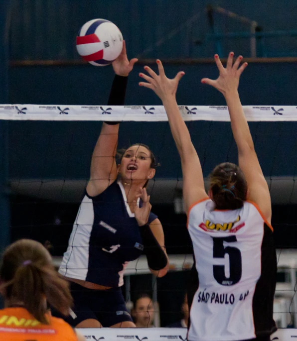 two women in uniforms reaching to hit a volleyball