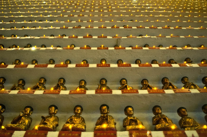 rows of buddhas on some shelves with candles in them