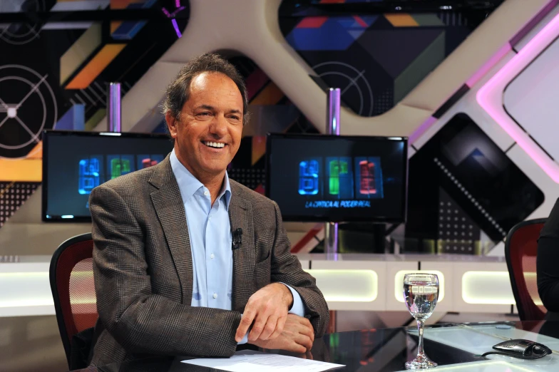 a man in a suit sits in front of a tv desk