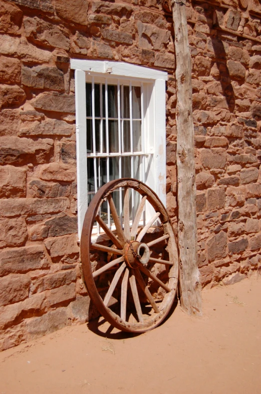 a old wooden wagon wheel sitting next to a brick wall