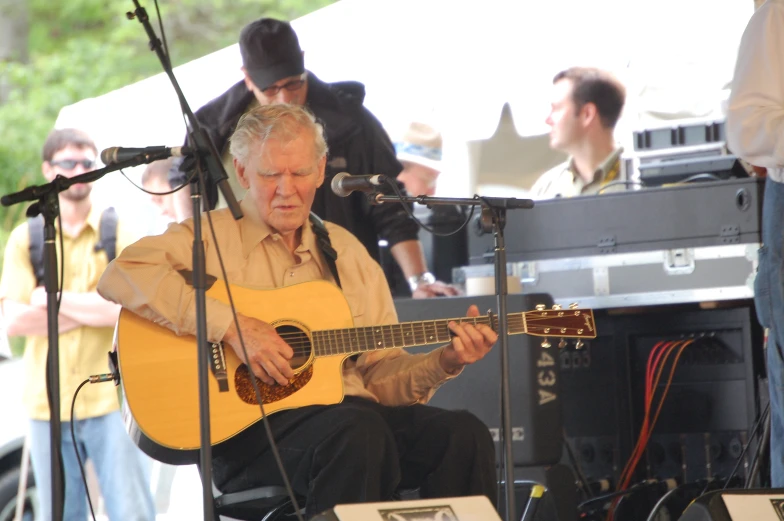 a man in tan shirt playing a guitar while others look on