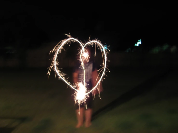 a person holds a sparkler heart in the dark