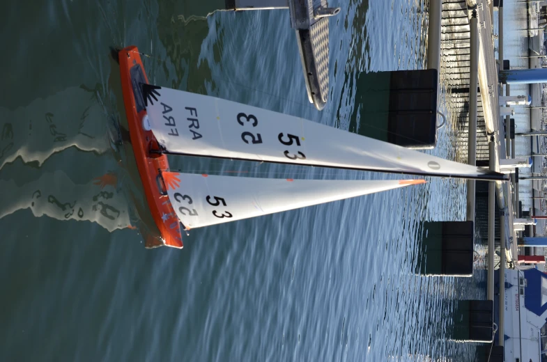 a boat with two white sails floating in a body of water