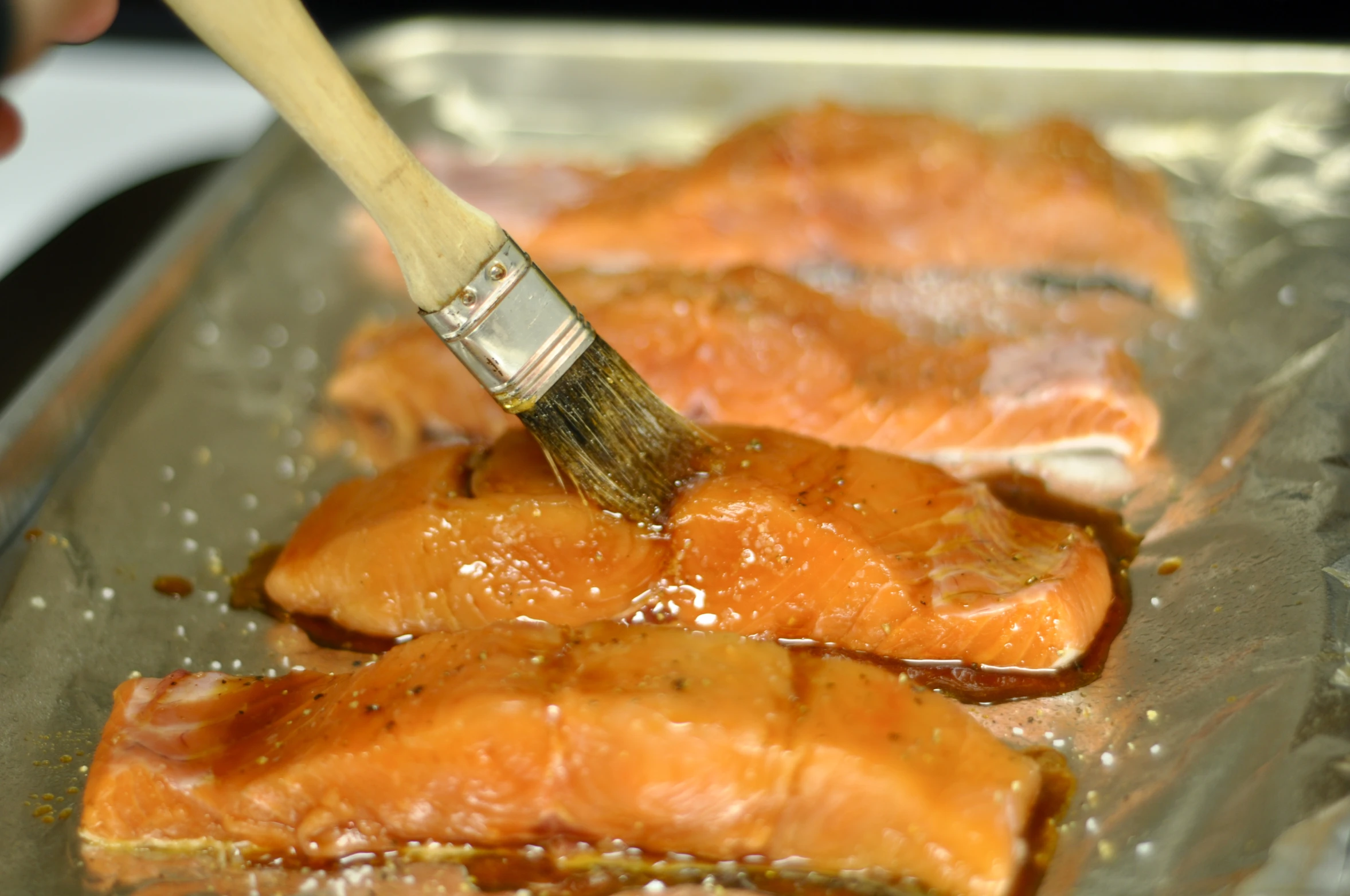 a brush brushing down salmon fillets on a tin foil baking tray