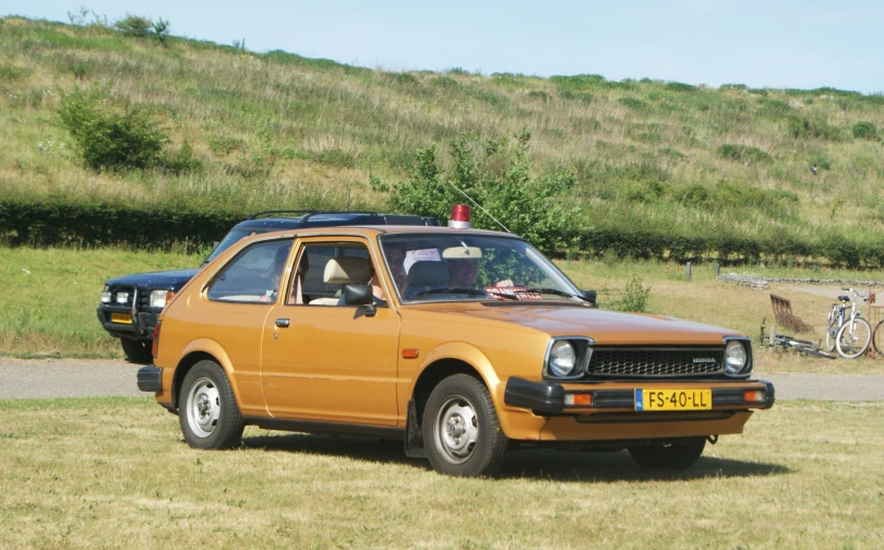 an orange taxi cab sitting in a green field next to other vehicles