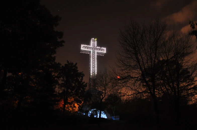 a large illuminated cross on top of a cross on a tree filled hill