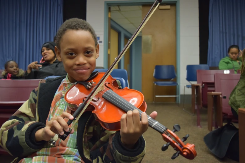 a boy playing an instrument in front of a classroom full of seated people