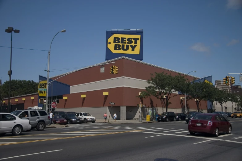 people walking across a busy street in front of a best buy store