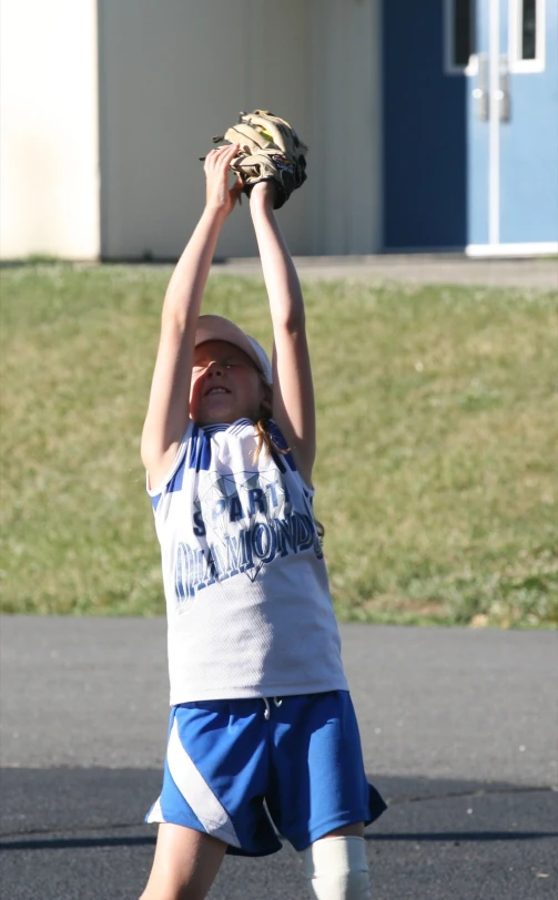 a little girl in a blue uniform throws a ball up in the air