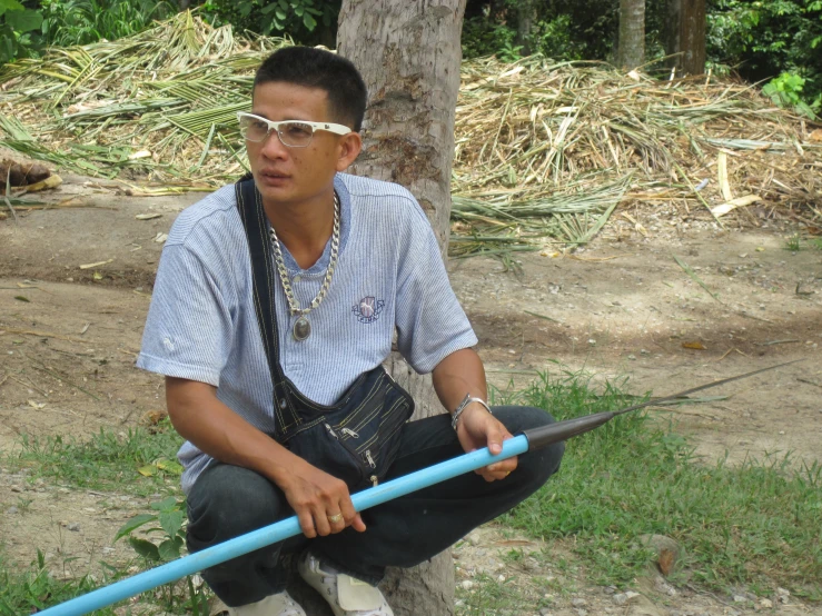 a man holding a blue object sitting next to a tree