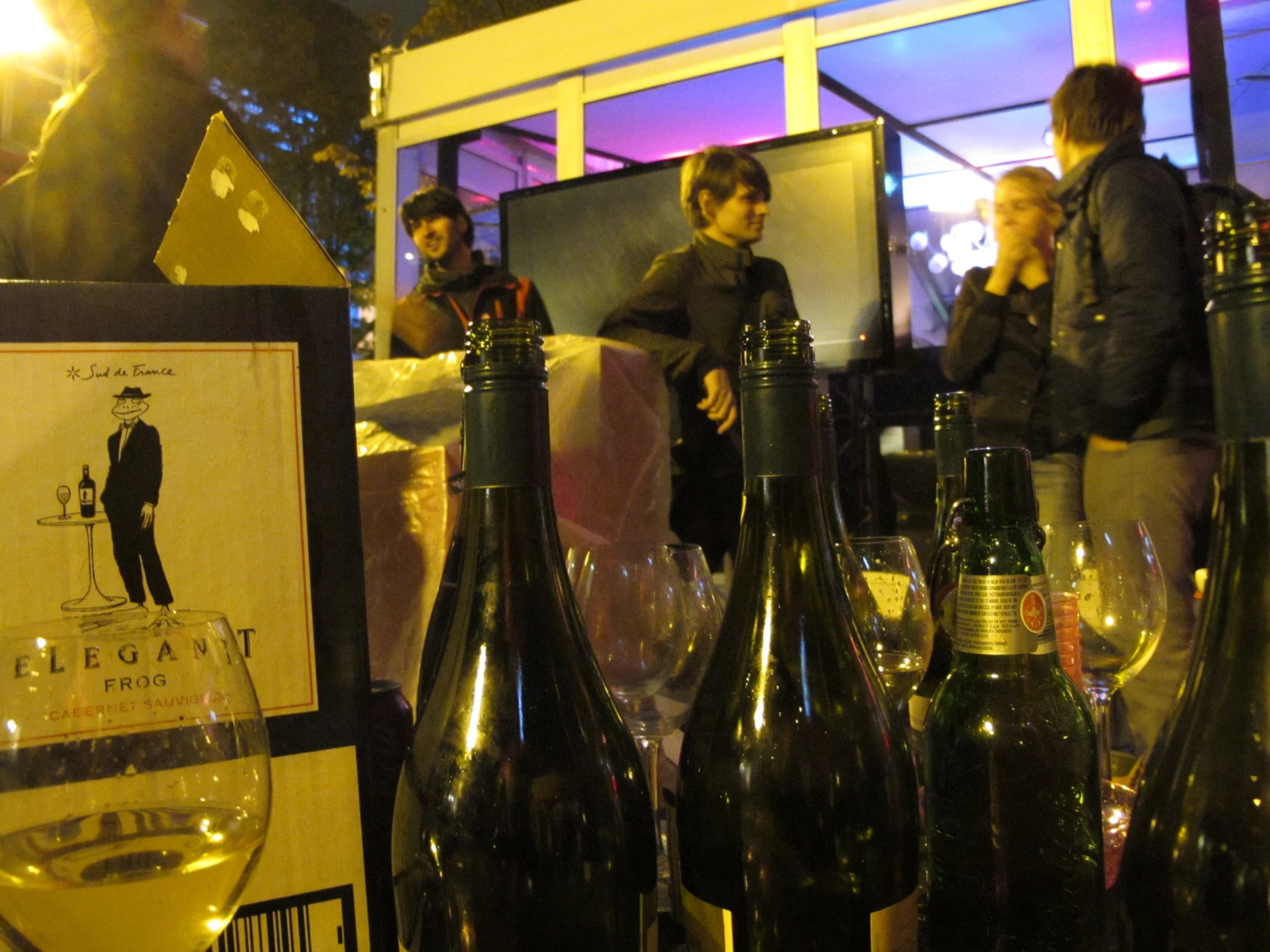 several people looking through bottles of wine in front of a window