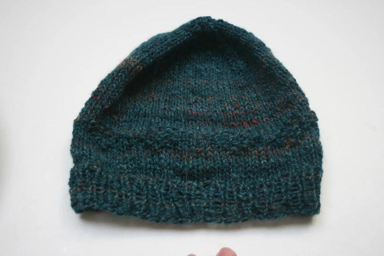 a hand wearing a knitted green hat with a red stripe