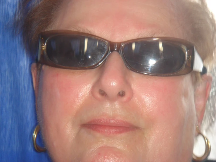 a woman with black sunglasses on, wearing gold hoop earrings and large round mirrored glasses