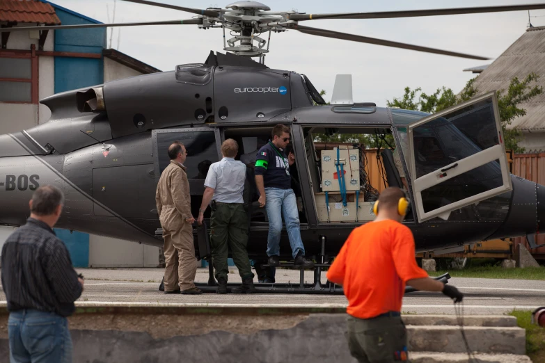 three men getting off a helicopter while another man looks on