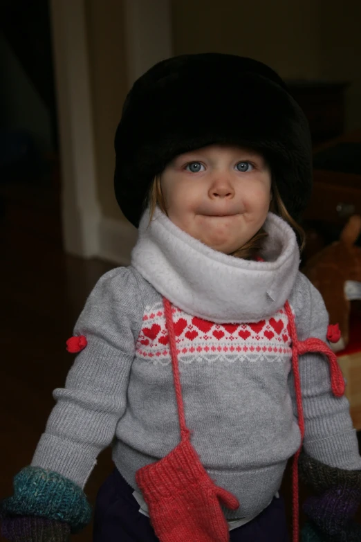 the child wears a gray sweater, green wool hat and holding a toy