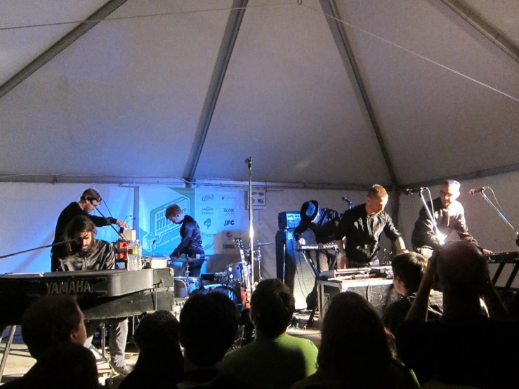 several people play instruments under a tent with an audience