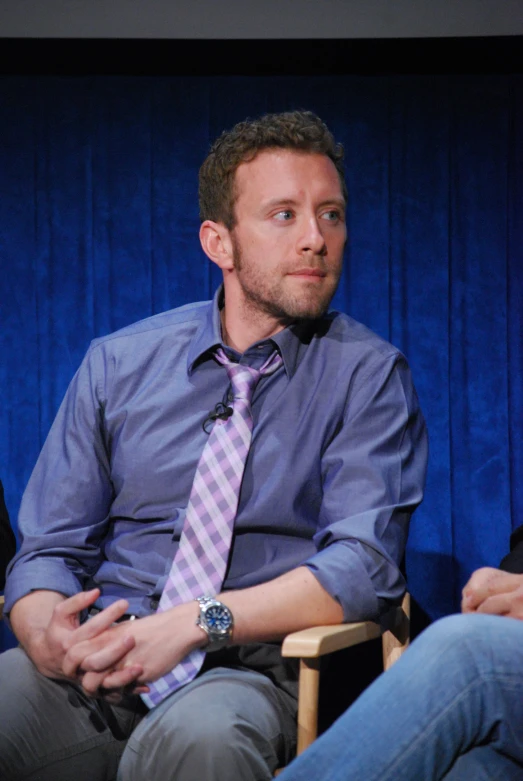 the man wearing a shirt and tie is sitting in a chair