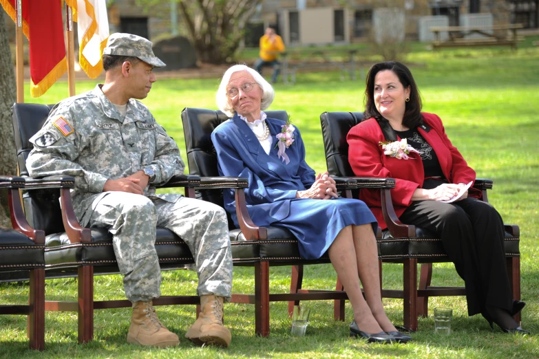 an old man sitting next to two women in military fatigues