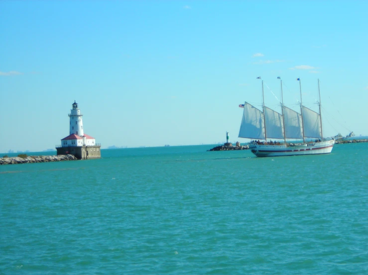 a large white sailboat in the water near a lighthouse