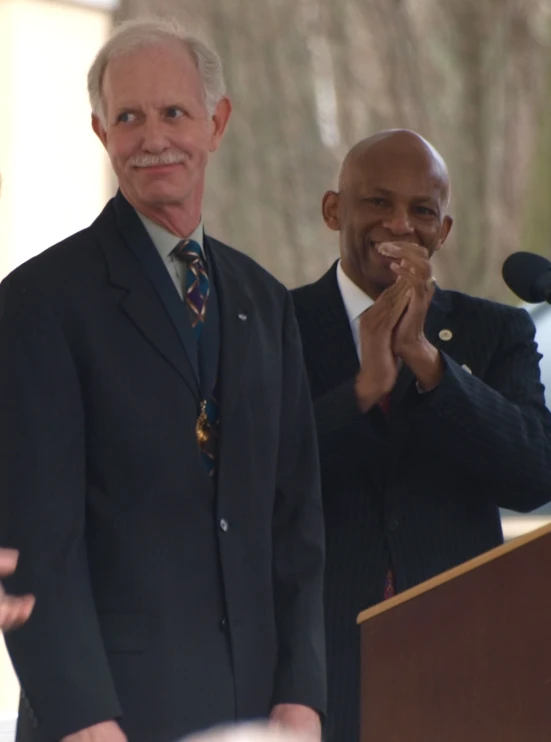 a man with white hair wearing a suit stands at a podium