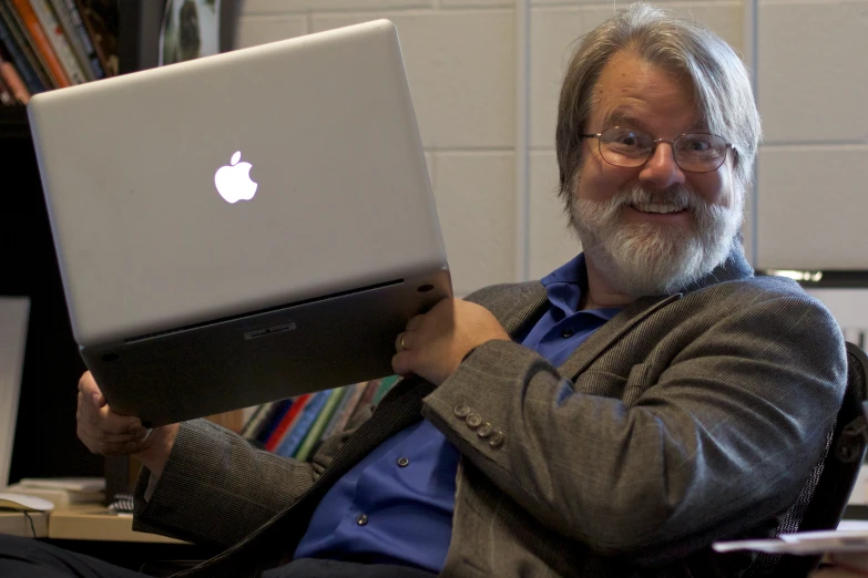 a man in his office holding a laptop with an apple logo