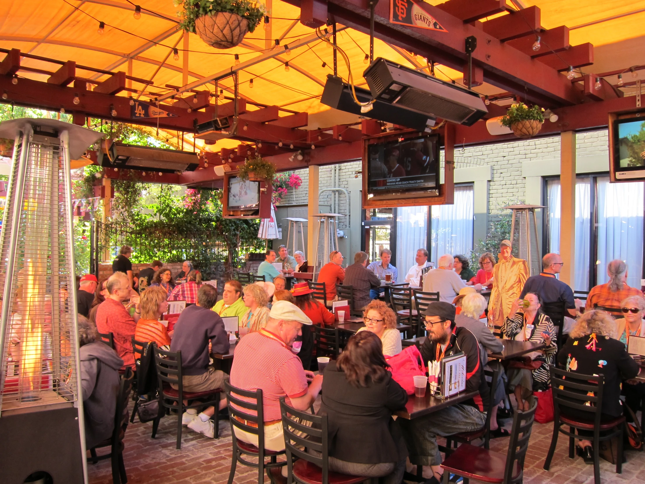 an outdoor restaurant with many people sitting at tables, and potted plants