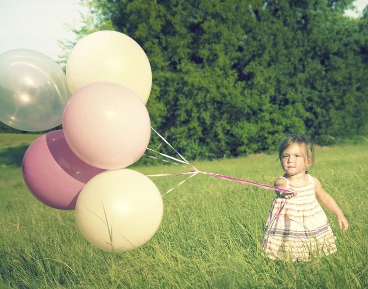 a little girl standing in tall grass with balloons