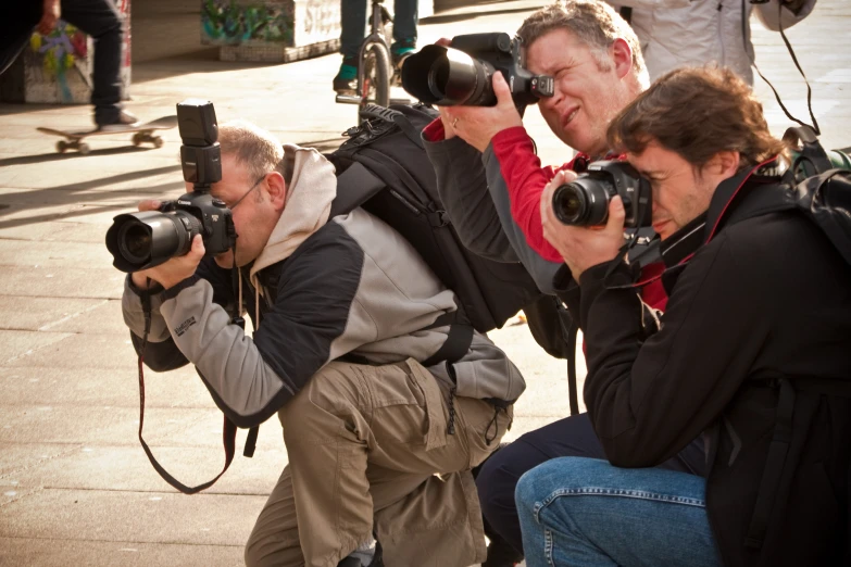 three people sit in the street, taking pictures with cameras